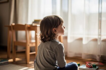 Enfant pensif près d'une fenêtre baignée de lumière naturelle, dans un salon familial accueillant