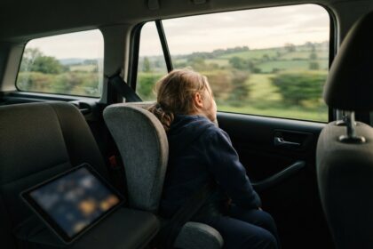 Un enfant assis à l'arrière d'une voiture regarde la campagne défiler par la vitre, une tablette posée devant lui
