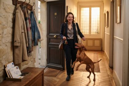 Une femme rentre chez elle, clés à la main, et son chien fauve saute vers elle dans le couloir