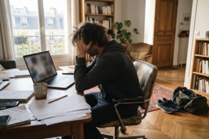 Homme assis à un bureau dans un salon, baskets et sac de sport posés au sol derrière lui