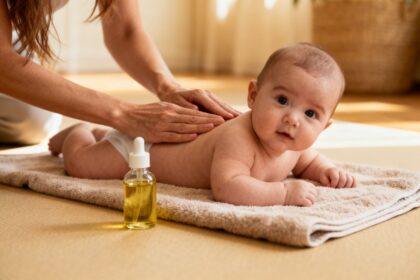 Mains d'une mère massant le dos d'un bébé allongé sur une serviette, un flacon d'huile à côté