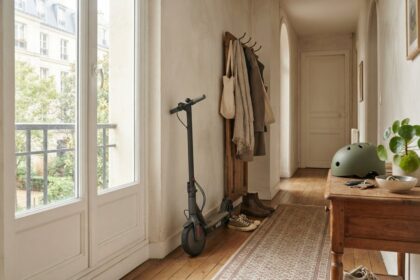 Trottinette électrique noire posée dans l'entrée d'un appartement, près d'un portemanteau et d'un casque vert
