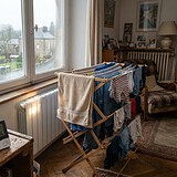 Étendoir en bois chargé de linge près d'un radiateur, vitre embuée et hygromètre affichant 68 % d'humidité